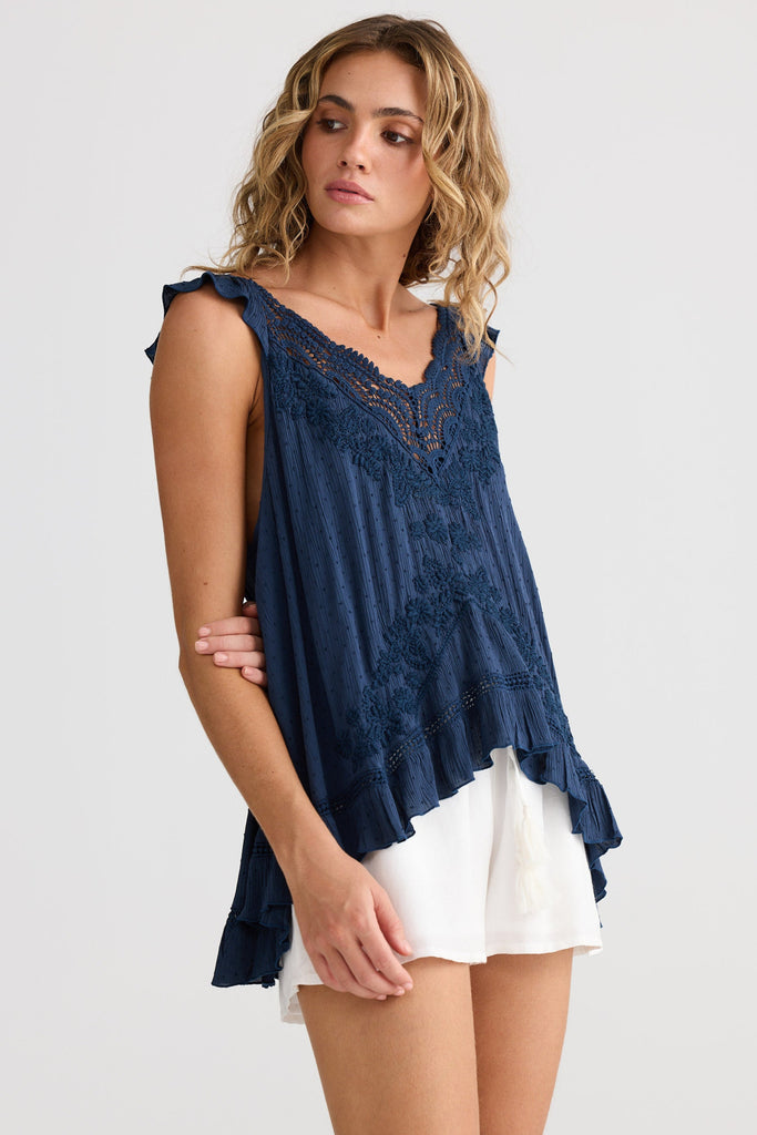 Woman wearing a navy blue sleeveless top with lace details and white shorts on a light gray background