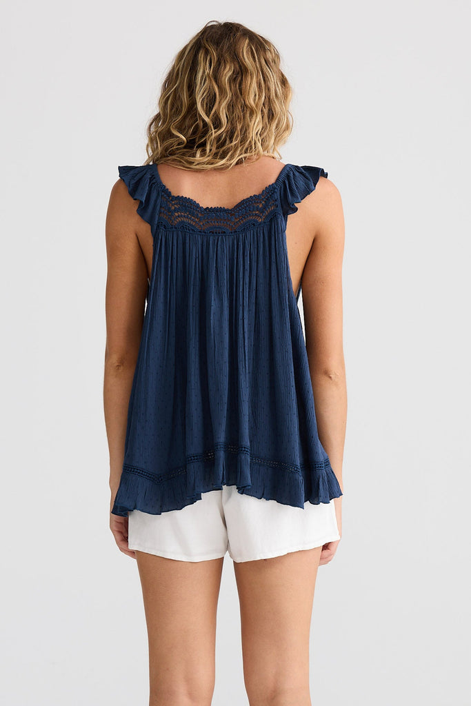 Person wearing a navy blue sleeveless top with lace details, white shorts, and beige boots on a white background