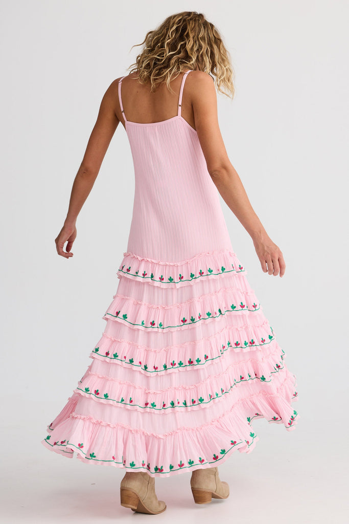 Woman wearing a pink dress with tiered ruffles and floral embroidery on a white background
