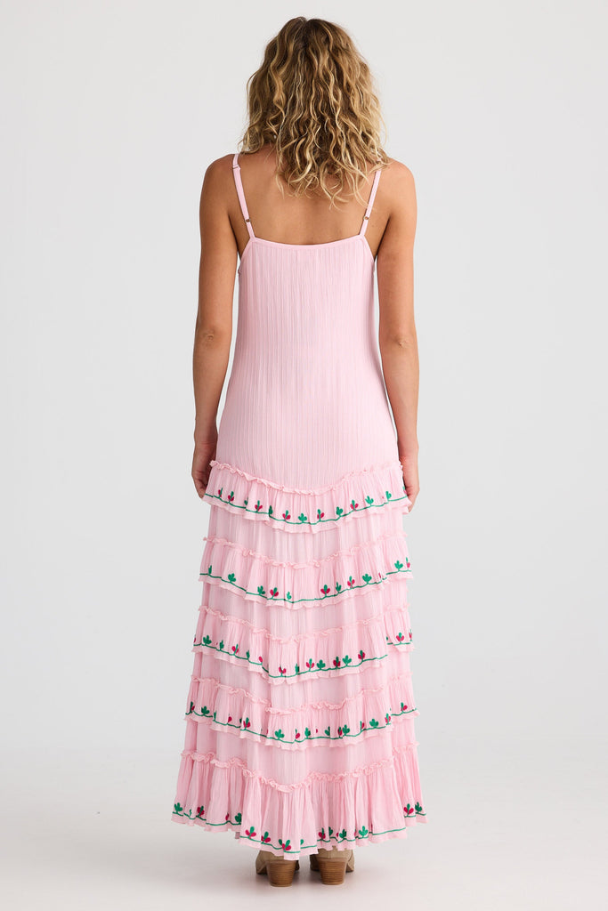 Woman wearing a pink tiered dress with floral details on a white background