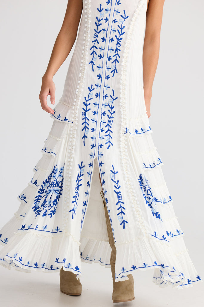White outfit with blue floral embroidery on a plain background
