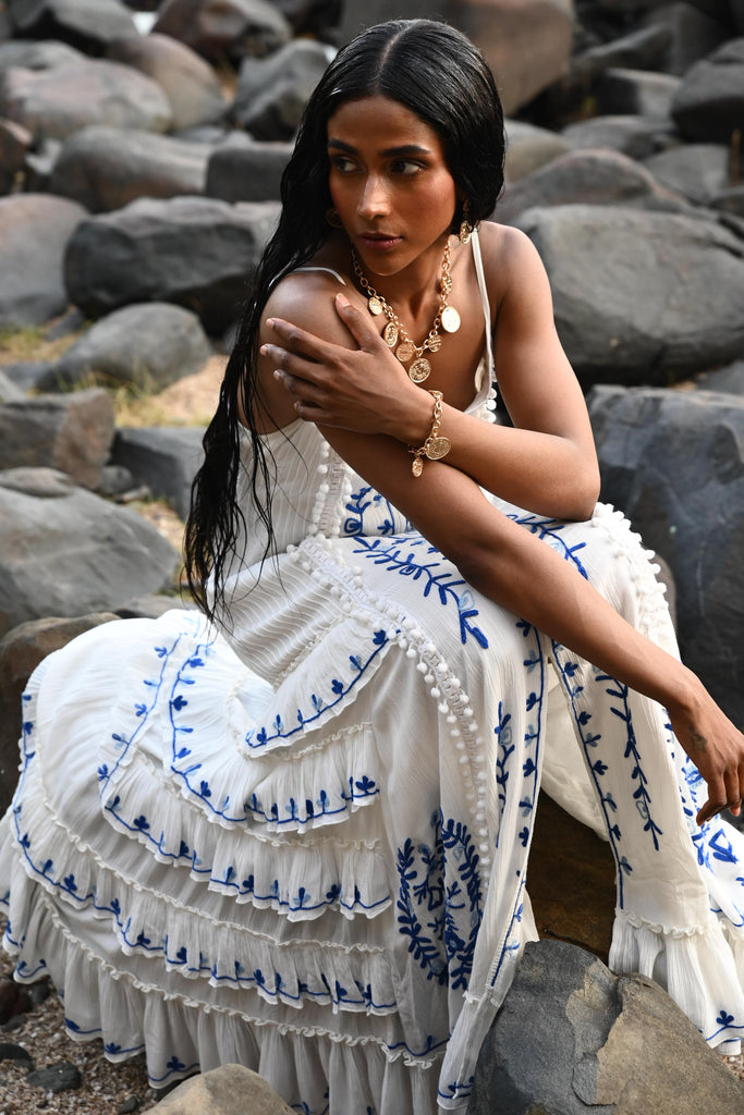 Woman in a white dress with blue patterns sitting on rocks.