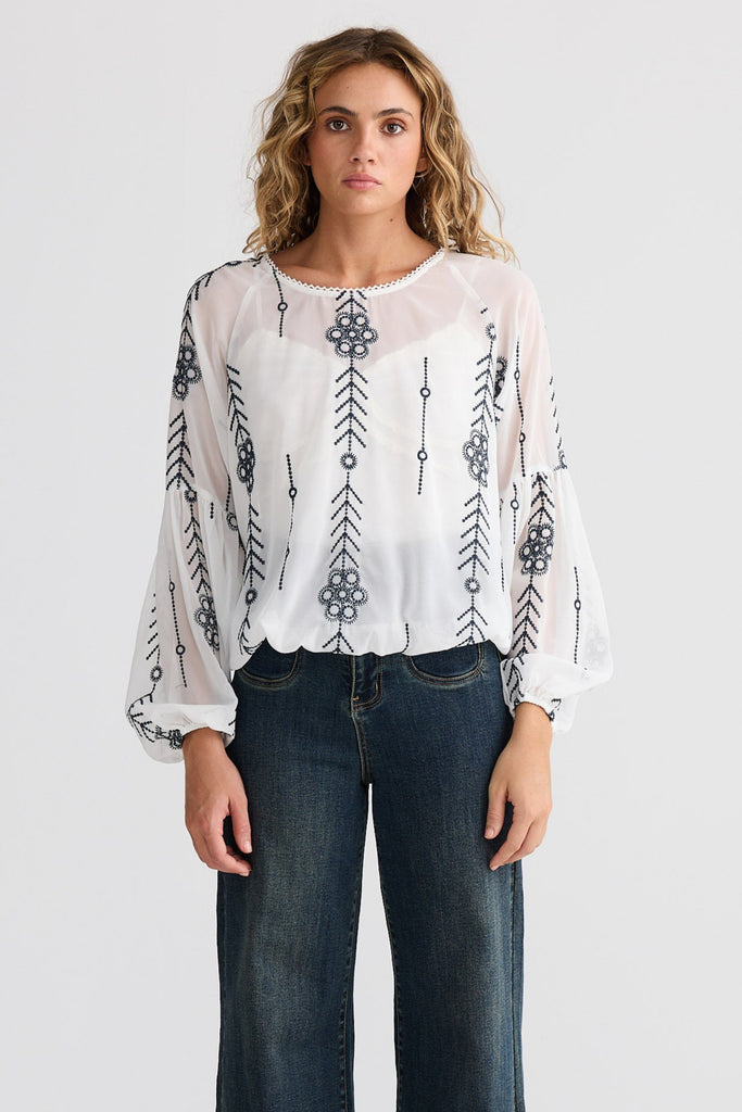 Woman wearing a white blouse with black patterns and dark blue jeans on a white background