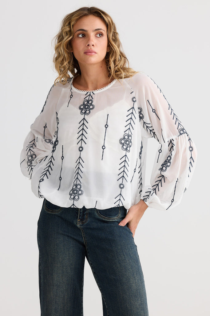 Woman wearing a white blouse with black floral and arrow patterns on a plain background