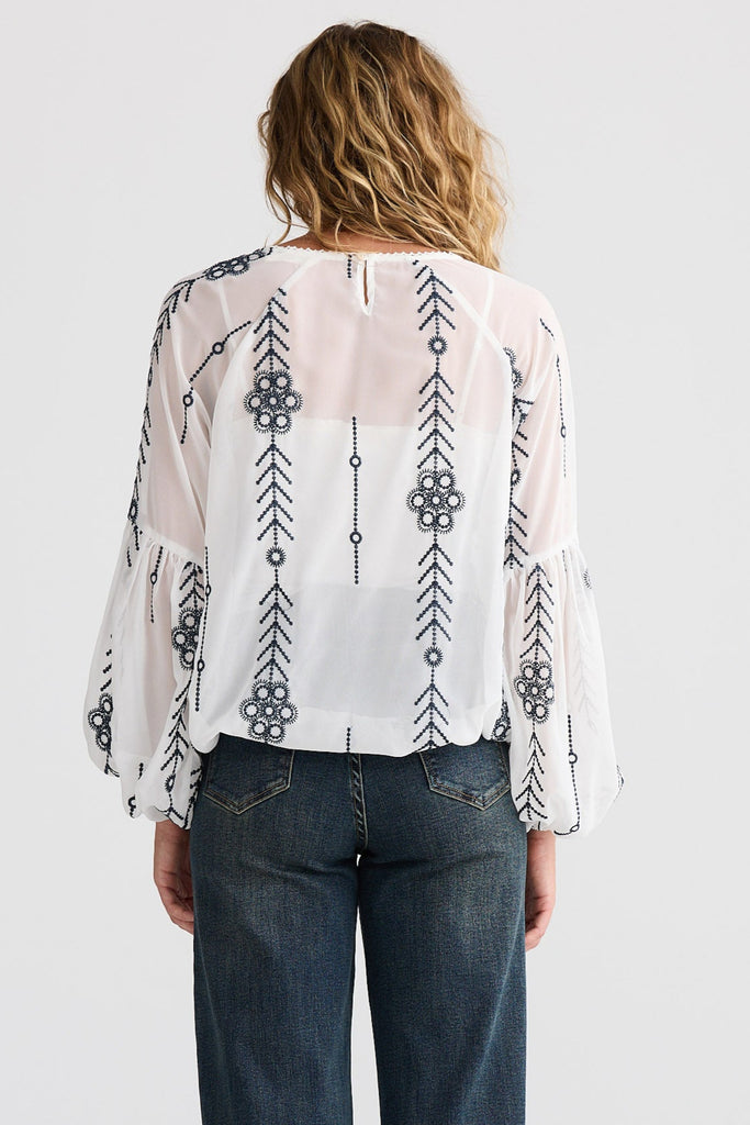 Person wearing a patterned blouse and blue jeans on a white background