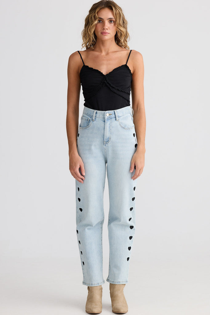 Woman wearing a black top and light blue jeans with heart patterns on a white background