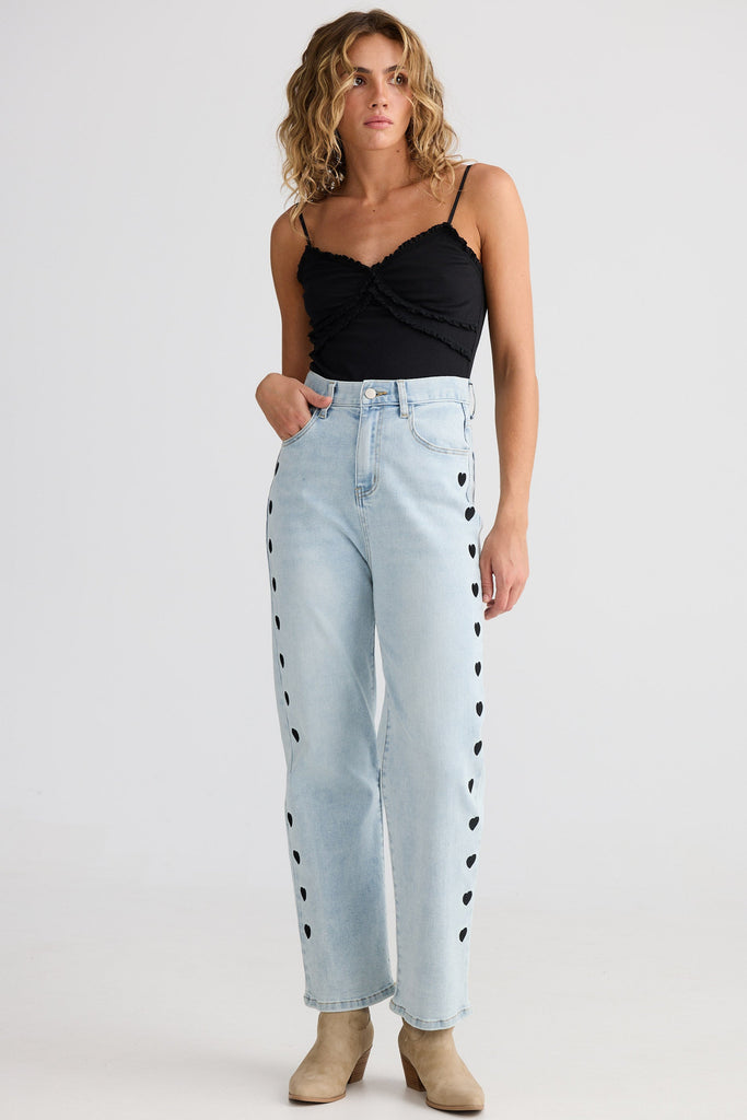 Woman wearing light blue jeans with black heart patterns and a black top on a white background