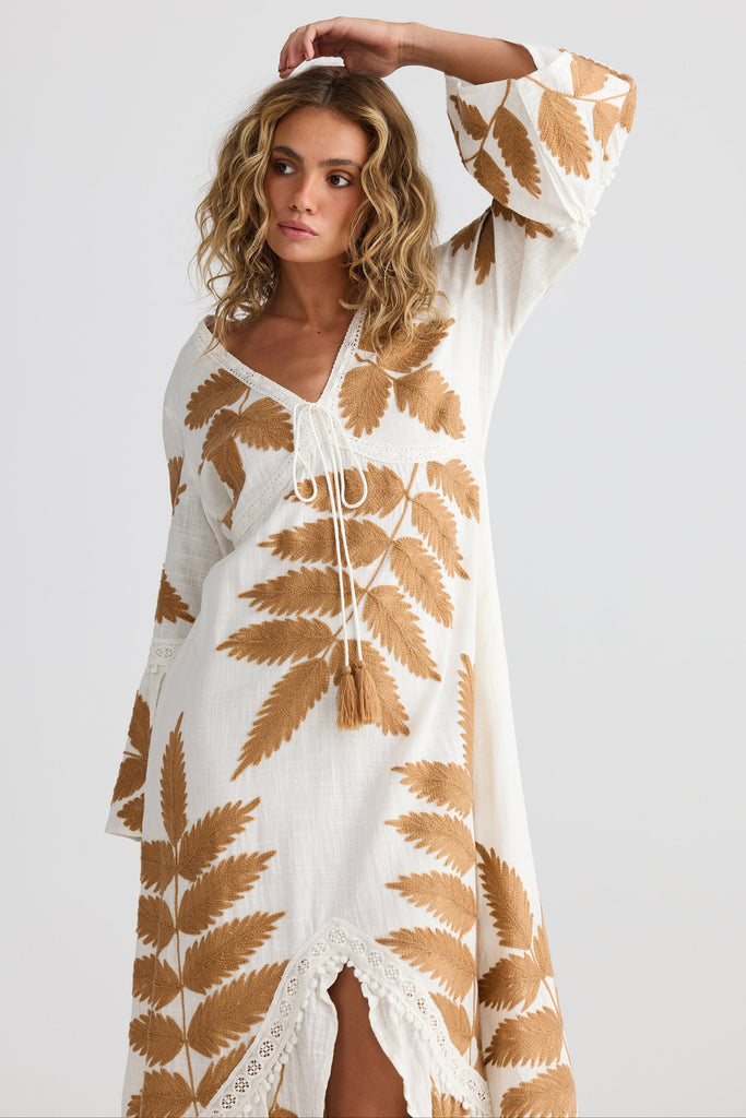 Woman wearing a white dress with brown leaf patterns on a plain background