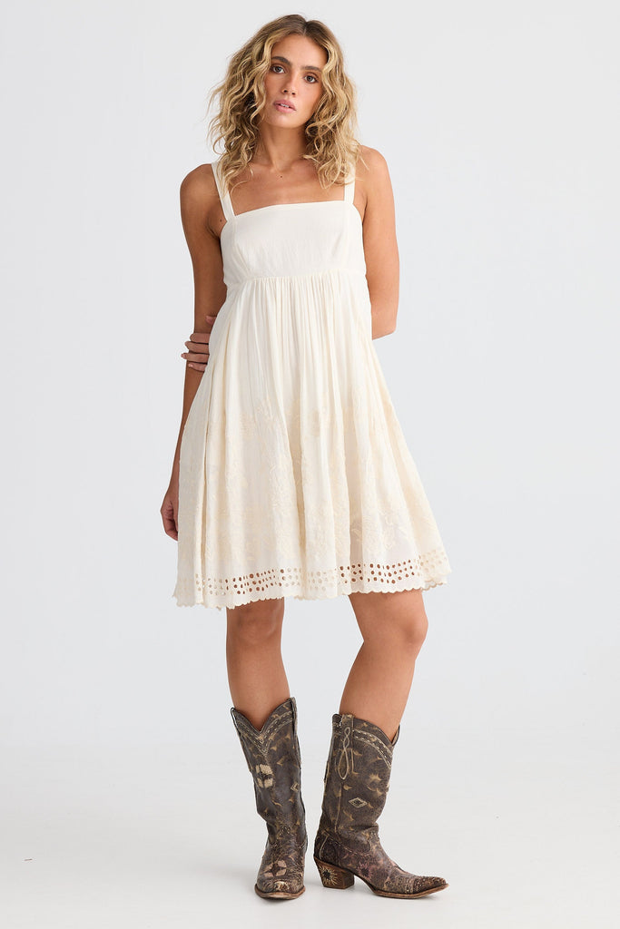 Woman wearing an off white dress and brown boots on a white background