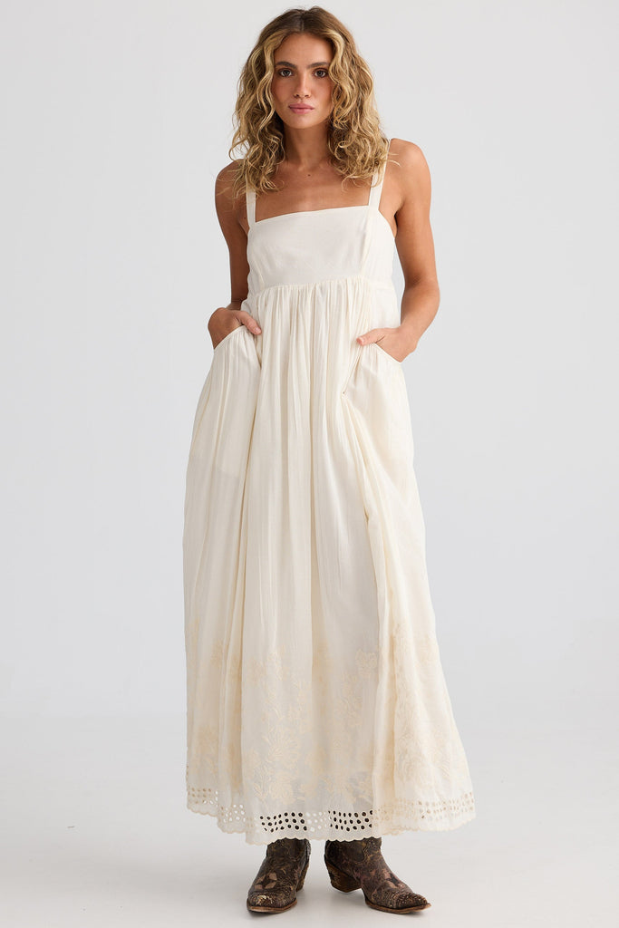 Woman wearing an off white dress with brown shoes on a white background