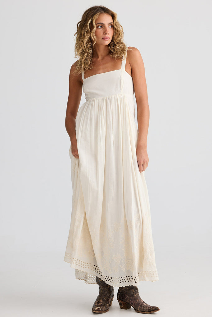 Woman wearing an off white dress with brown boots on a plain background