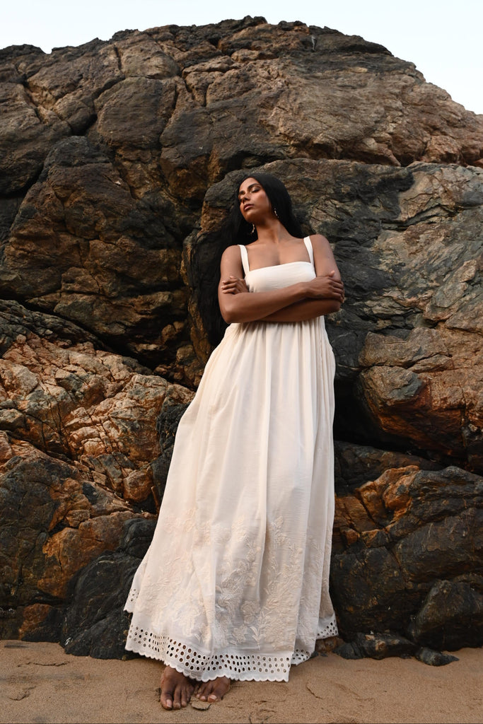 Person in an off white dress standing against a large rock formation with a light blue background