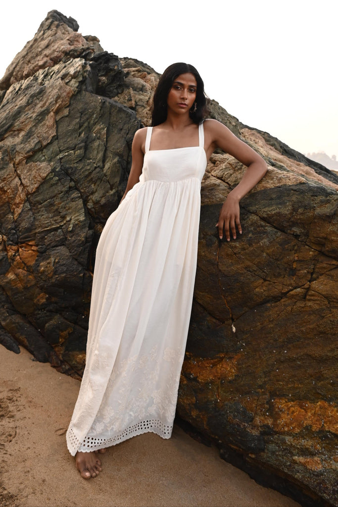 Woman in an off white dress leaning on a rocky surface