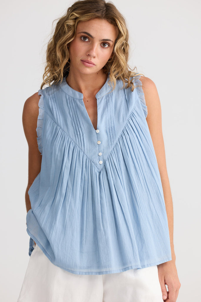 Woman wearing a light blue sleeveless blouse with buttons on a white background