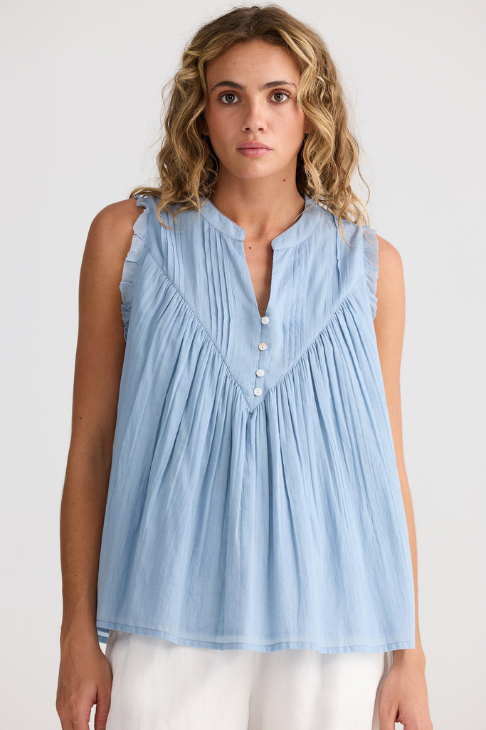 Woman wearing a light blue sleeveless blouse with buttons on a white background