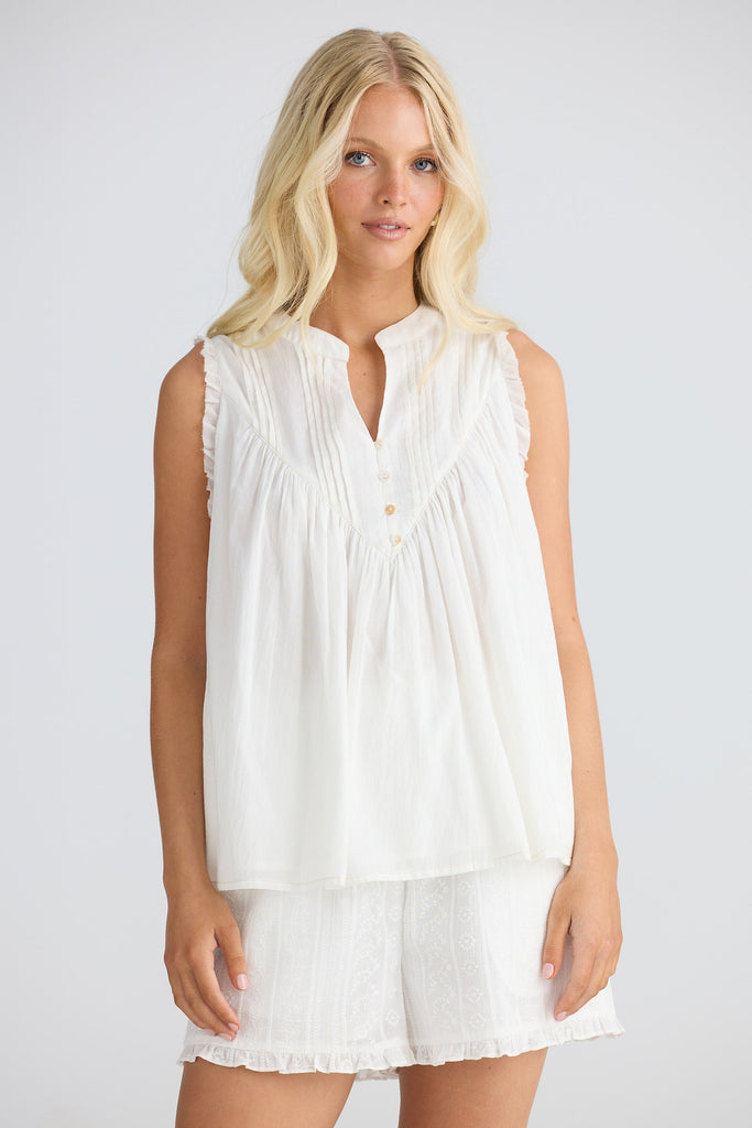 Woman wearing a white sleeveless top and shorts on a plain background