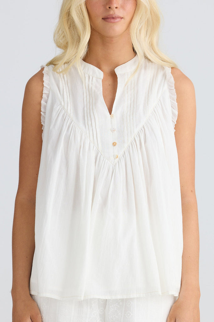 Woman wearing a white sleeveless top and shorts on a plain background