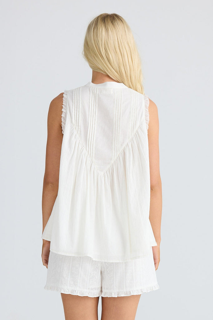 Person wearing a white sleeveless top and shorts on a plain background