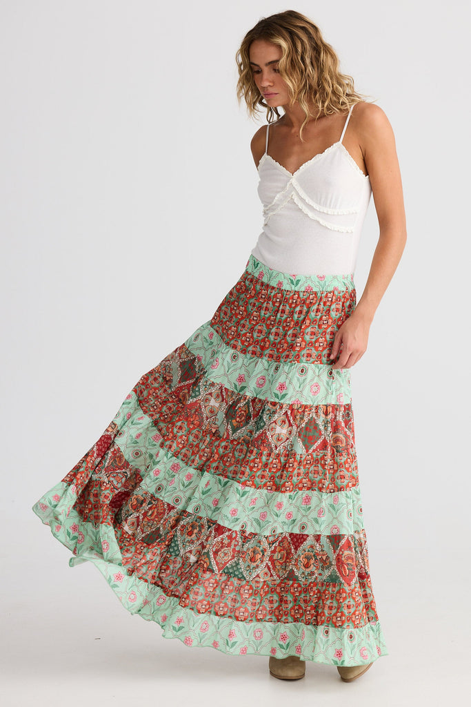 Woman wearing a long, patterned skirt with a white top on a white background