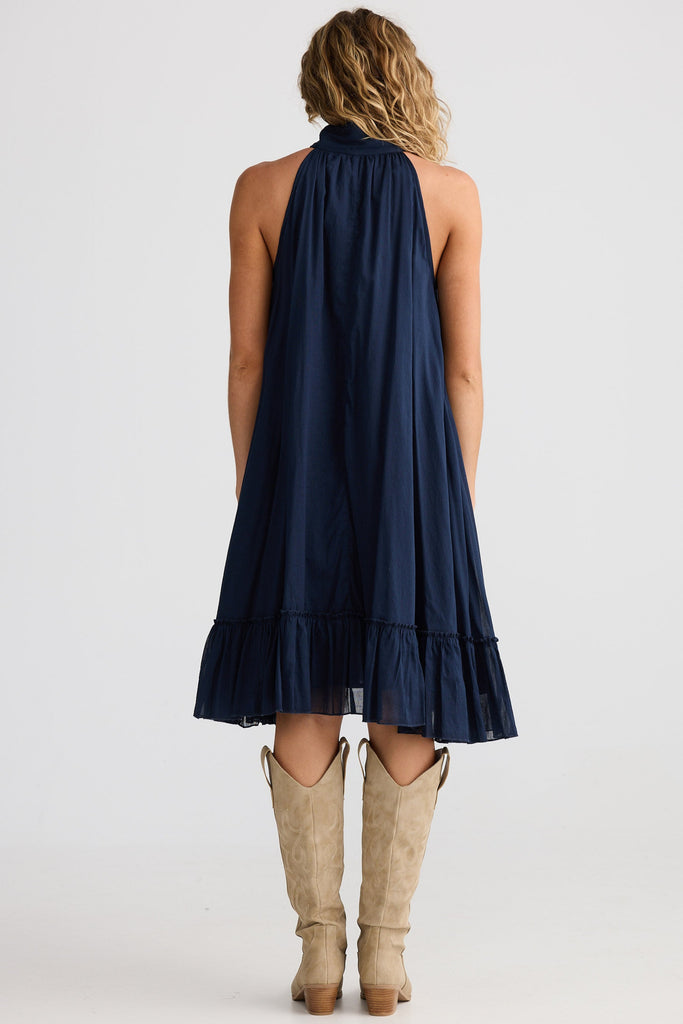 Woman wearing a navy halter dress with beige boots on a white background