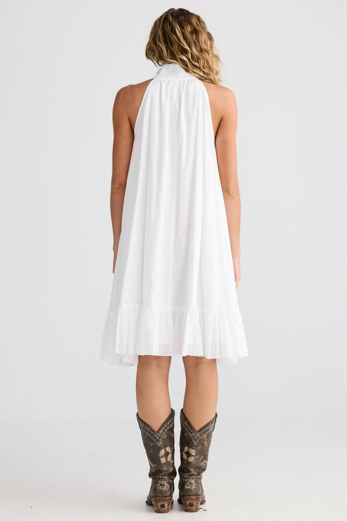 Woman wearing a white halter dress and cowboy boots on a plain background