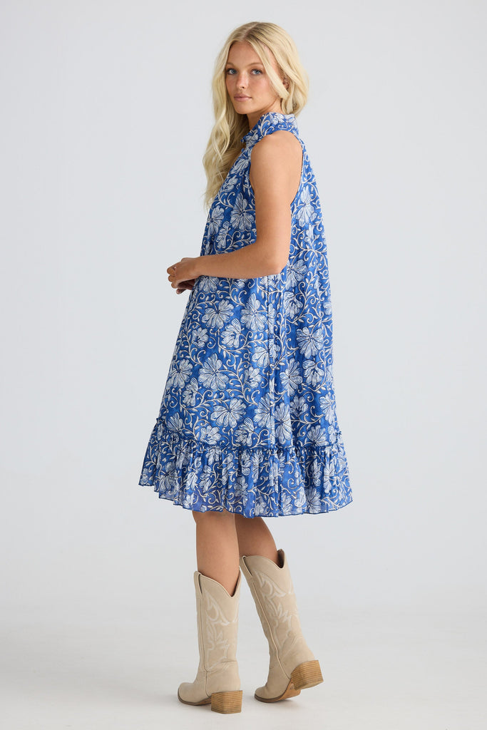 Woman wearing a blue floral dress with beige cowboy boots on a white background