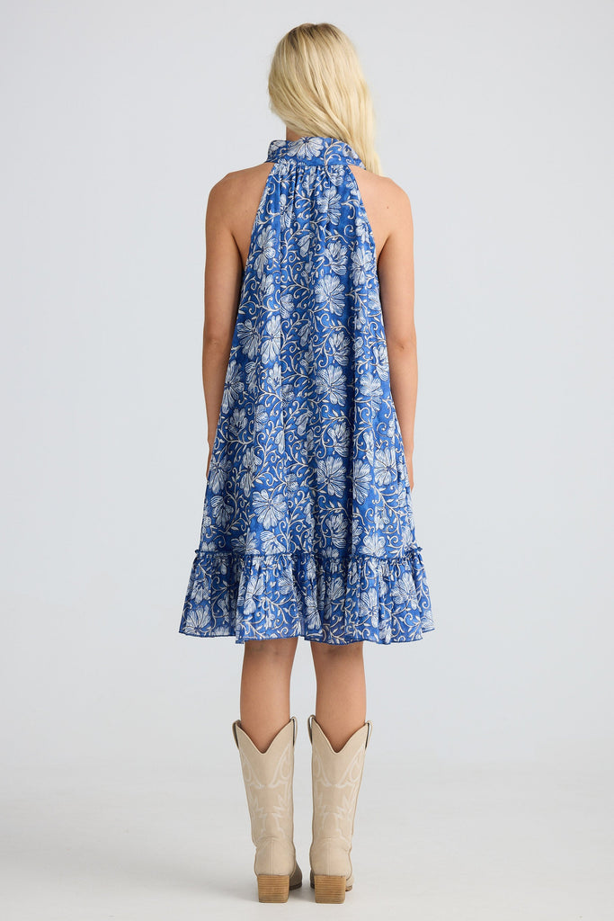 Woman wearing a blue floral dress with beige cowboy boots on a white background