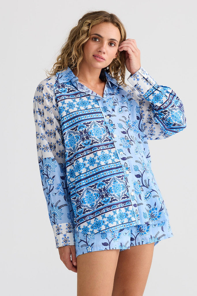 Woman wearing a blue patterned shirt and  shorts with beige knee-high boots on a white background