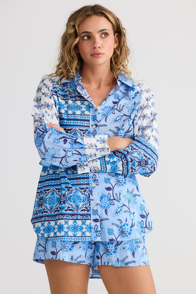 Woman wearing a blue patterned shirt and shorts set on a light gray background