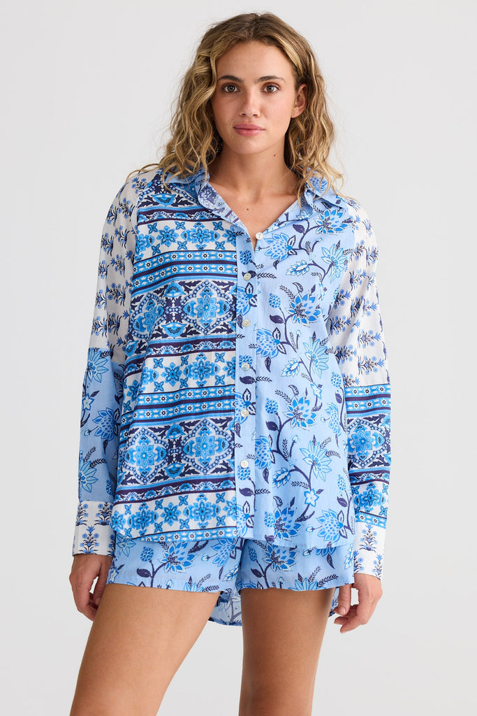 Woman wearing a blue patterned shirt and shorts on a white background