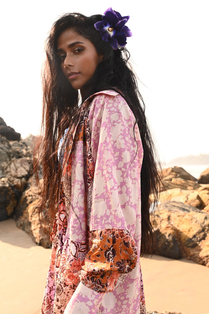 Woman wearing a pink floral shirt with a purple flower in her hair, standing on a beach.