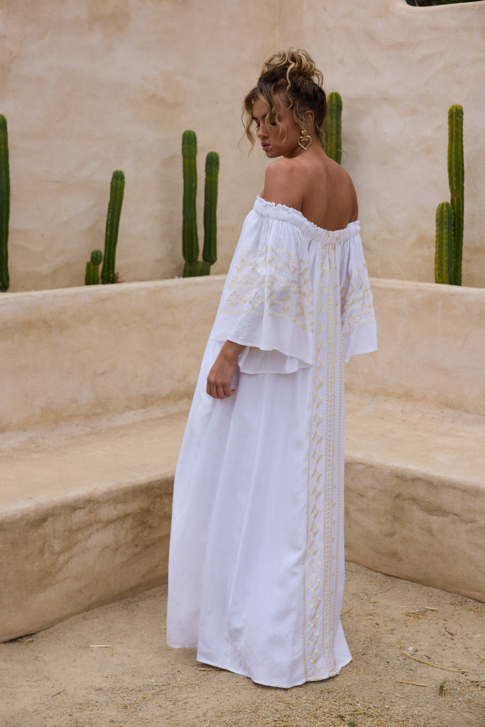 Woman in a white off-shoulder dress standing in front of cacti.