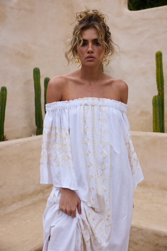 Woman in a white off-shoulder dress standing in front of cacti.