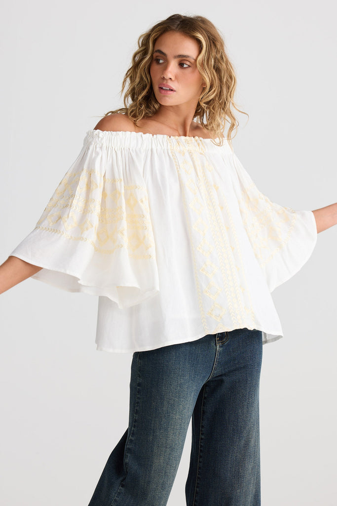Woman wearing a white off-shoulder top and blue jeans on a white background