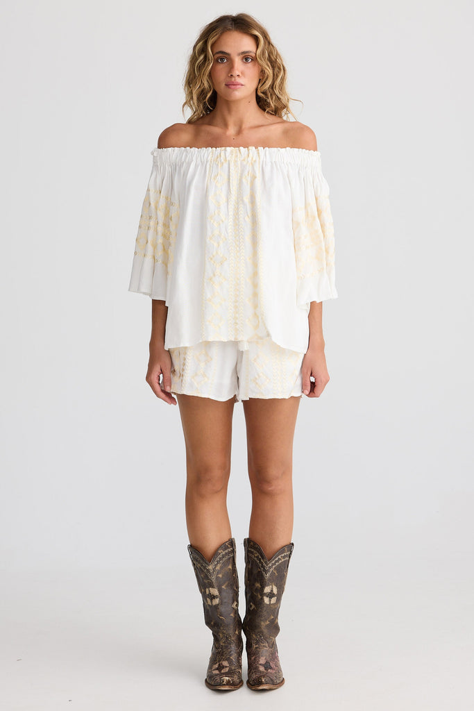 Woman wearing a white off-shoulder top and shorts with cowboy boots on a white background