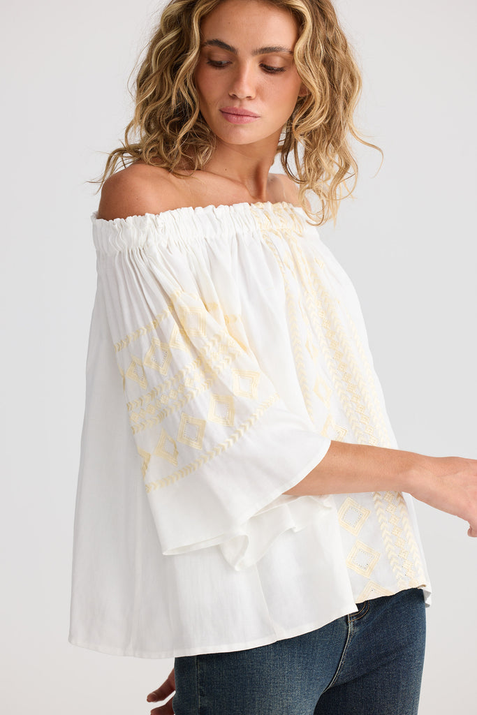 Woman wearing a white off-shoulder top with cream pattern on a plain background