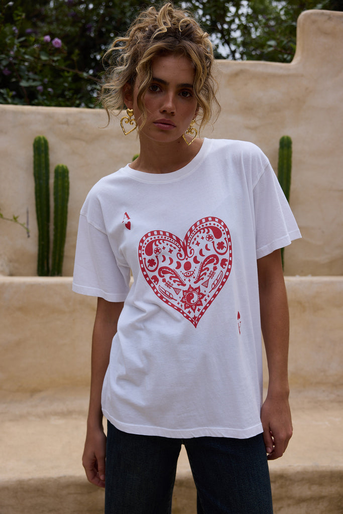 Woman wearing a white t-shirt with a red heart design outdoors.