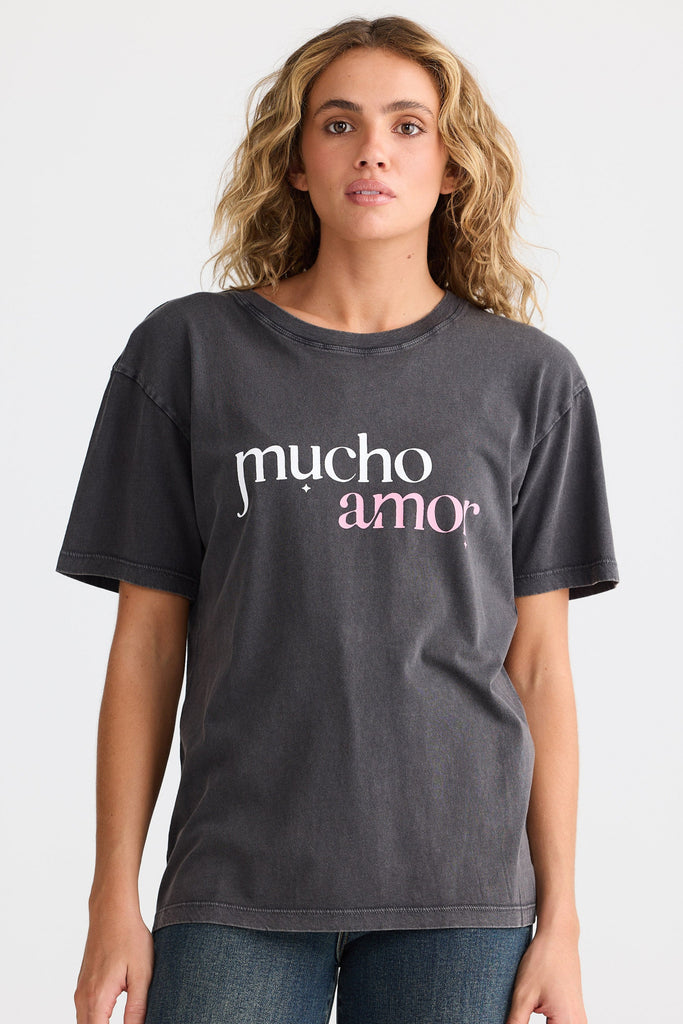Woman wearing a dark gray t-shirt with 'mucho amo' text on a light gray background