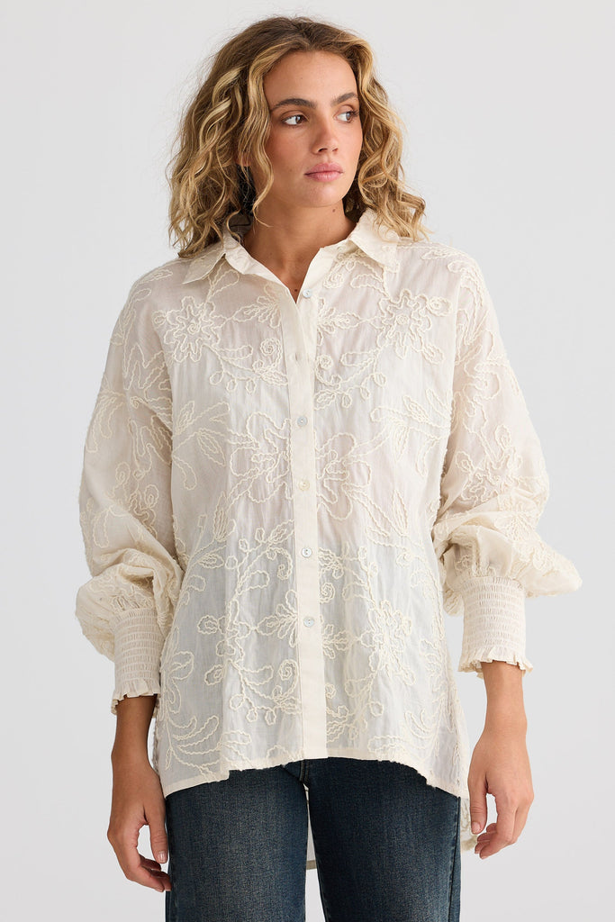 Woman wearing a cream embroidered shirt and jeans on a white background