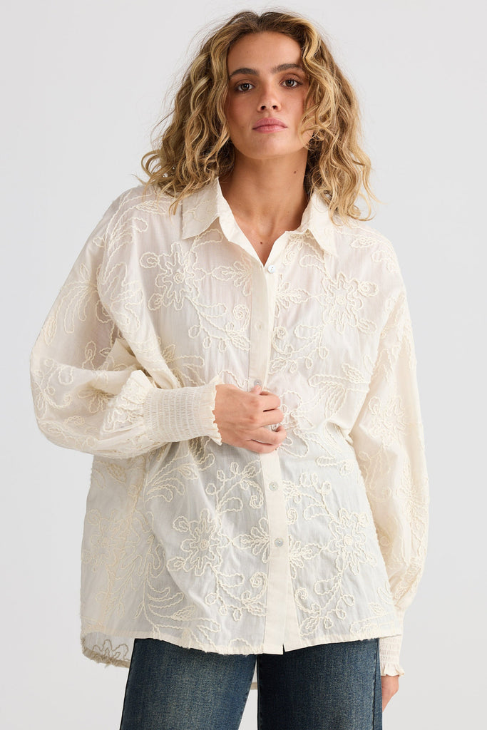 Woman wearing a natural embroidered blouse and jeans on a light gray background