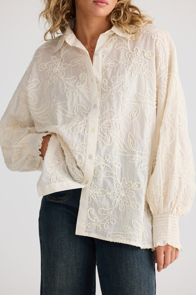 Woman wearing a cream embroidered shirt with long sleeves on a white background