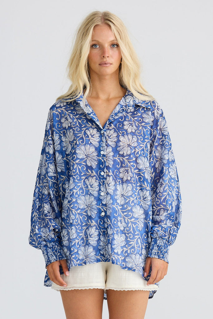 Woman wearing a blue floral blouse, white shorts, and beige boots on a white background