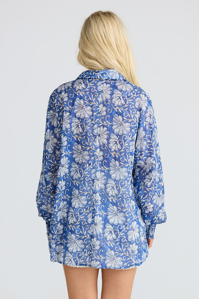 Person wearing a blue floral shirt and beige cowboy boots on a white background