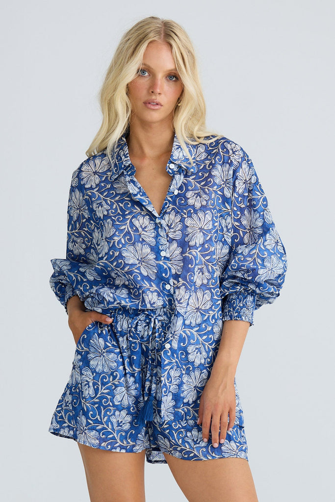 Woman wearing a blue floral outfit with beige cowboy boots on a white background