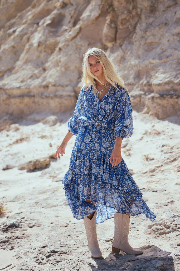 Woman in a blue floral shirt and skirt standing in a desert landscape