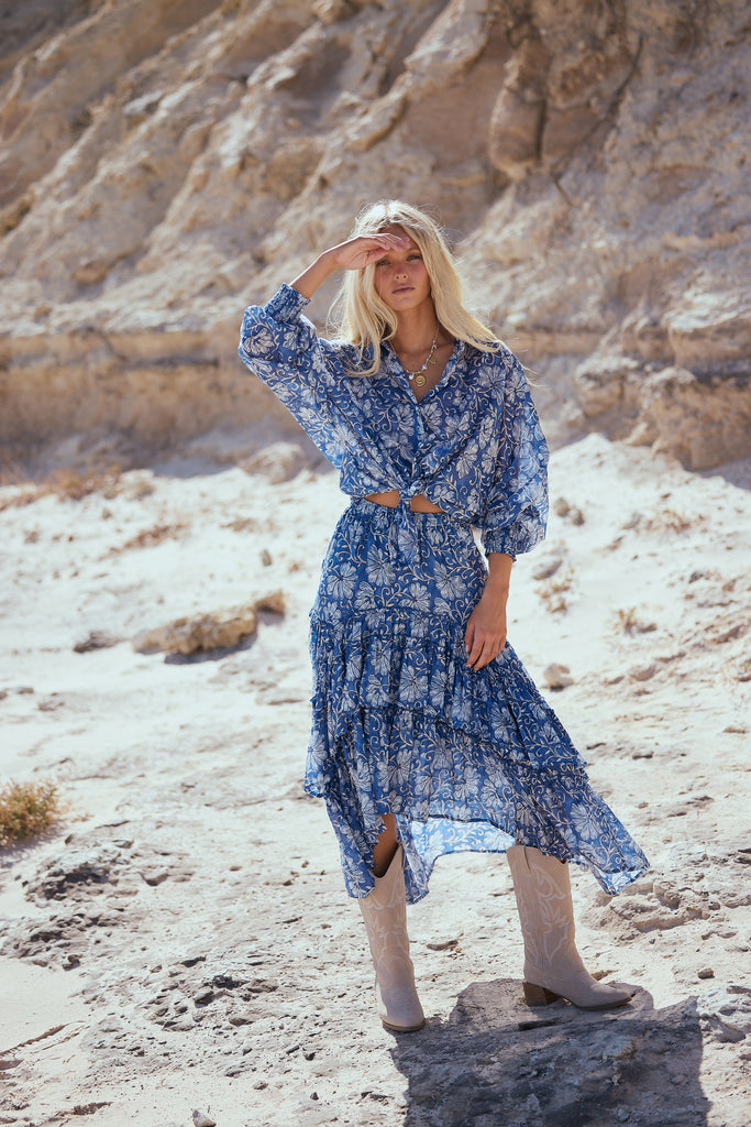 Woman in a blue floral shirt and skirt standing in a desert landscape