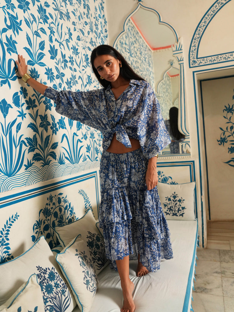Woman in a blue patterned outfit standing in a room with floral wallpaper.