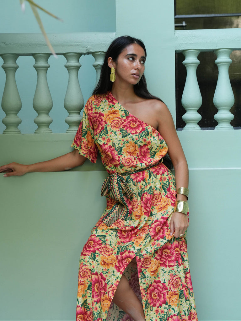 Woman wearing a colorful floral dress standing against a light green wall.