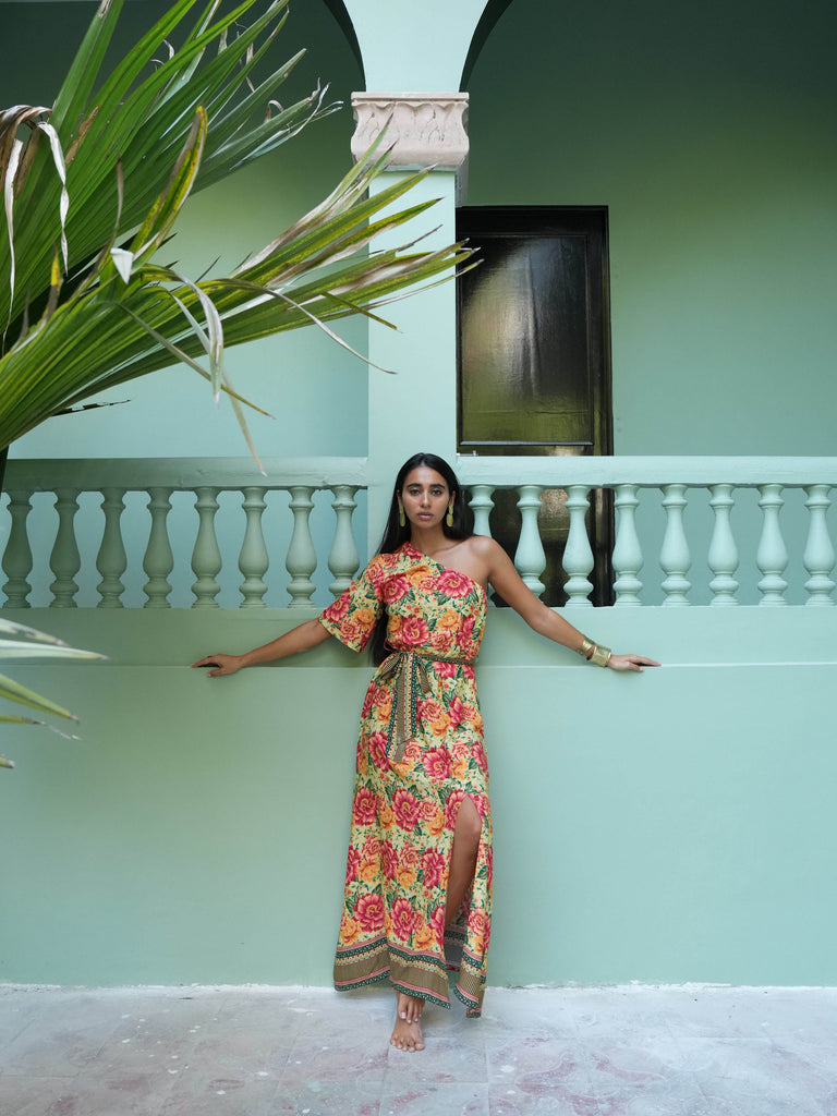 Woman in a floral dress standing in front of a light blue wall with a plant to the left.