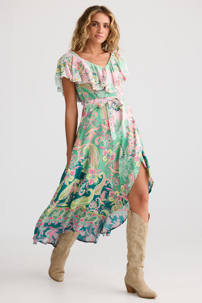 Woman wearing a floral dress with a high slit and beige knee-high boots on a white background